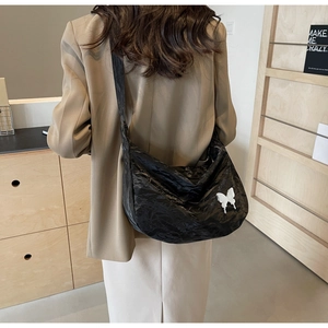 Détail du sac bandoulière plissé noir avec un papillon 3D blanc sur une matière texturée