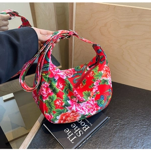 Detailed view of red peony floral hobo bag with adjustable strap on a dark surface