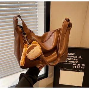 Detail of a brown leather hobo bag with a sweet plush charm and lychee texture finish