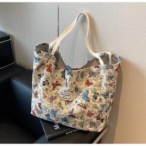 Detailed close-up of large canvas tote bag with vibrant butterfly print on black leather sofa