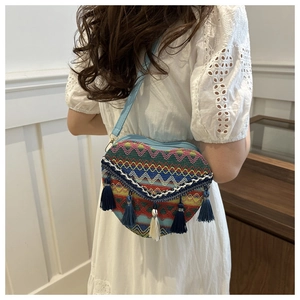 Detail of colorful woven heart bag with ethnic patterns and tassels on white lace dress