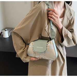 Detail of light green baguette bag with landscape print and decorative floral metal chain