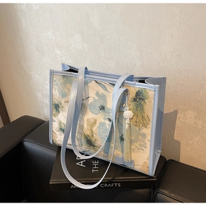 Détail du cabas en toile florale avec bordure en cuir bleu clair et pompon décoratif