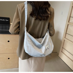 Détail du sac croissant en satin bleu clair avec emblème papillon argenté et sangle