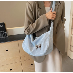 Détail du sac croissant bleu clair avec boucle papillon argentée sur une tenue marron
