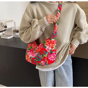 Detail of red floral shoulder bag with phoenix pattern worn on a beige sweatshirt