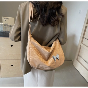 Gros plan du sac bandoulière abricot avec texture froissée et pendentif papillon argenté