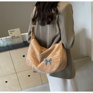 Détail d'un sac demi-lune beige avec texture plissée et boucle papillon argentée