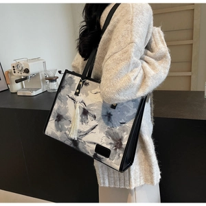 Détail du sac cabas en toile avec motif floral gris-bleu et pompon blanc sur l'épaule