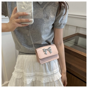 Détail d'un mini sac bandoulière rose avec un nœud argenté décoratif et bandoulière chaîne
