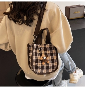 Detailed back view of a checkered woven crossbody bag with a plush charm on a model