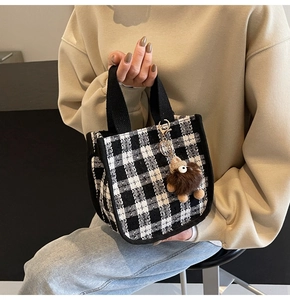 Detail of checkered tweed tote bag with black strap and a brown plush monster charm