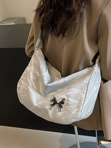 Sac hobo argenté avec détail papillon porté par un mannequin dans un cadre minimaliste