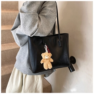 Close-up of a large black tote bag featuring soft leather texture and a cute bear charm