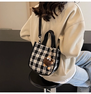 Rear view of a black and white plaid tweed handbag with a brown plush monster charm