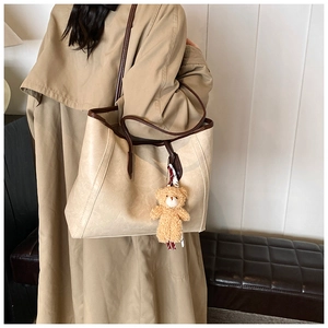 Detail of a large cream tote bag with brown straps and a cute plush bear pendant accessory