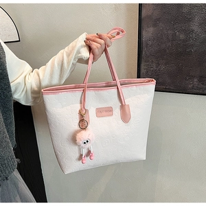 Detail of pink and white tote bag with embossed cartoon patterns and plush monster charm