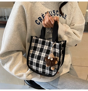 Detail of checkered tote bag with black webbing handles and a plush monster charm