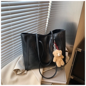 Detail view of large black tote bag with textured leather and cute plush bear charm