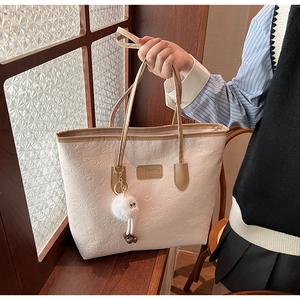 Detail of cream tote bag featuring cartoon embossed textures and a plush ball charm