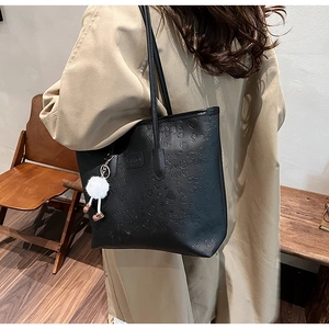 Detail of black embossed tote bag with cartoon patterns and white plush charm on model