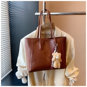 Detail of vintage brown tote bag with plush bear charm and scarf on blazer