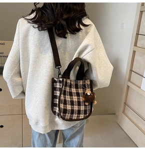 Detail of plaid mini tote bag with plush bear charm and adjustable strap worn by model