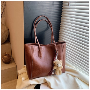 Detailed view of a brown vintage leather tote bag with a cute plush bear charm decoration