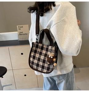 Detail of plaid crossbody bag with wide canvas strap and plush toy charm on a model