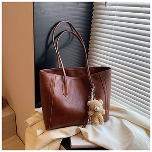 Detailed texture of brown tote bag with plush bear charm and ribbon against shutters