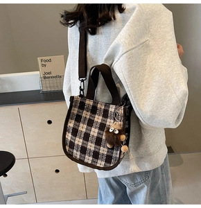 Detail of vintage checkered tote bag with brown straps and cute monster plush pendant