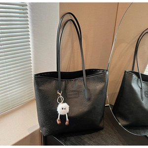 Close-up of black PU leather tote bag with embossed patterns and furry monster charm