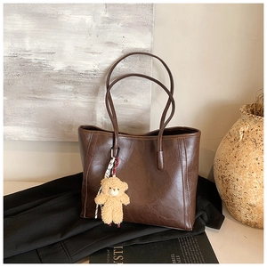Detail of deep brown tote bag with oily leather texture and plush bear pendant accessory