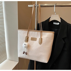 Detail of beige tote bag with cartoon embossing, fashion label, and plush doll charm
