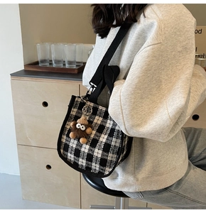 Detail of checkered canvas tote bag with adjustable black strap and cute plush doll pendant
