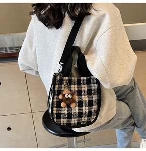 Detail of checkered canvas crossbody bag with a cute plush charm and black woven strap