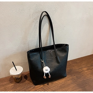 Detail of black tote bag featuring embossed heart patterns and a cute plush ball charm
