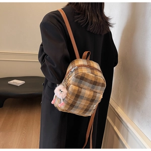 Plaid backpack with pink plush monster charm and leather straps shown on a model