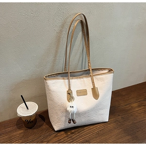 Detail of white embossed tote bag featuring fashion tag and cute plush pendant charm