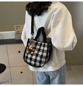 Detail of checkered canvas tote bag with brown plush monster charm on model's shoulder