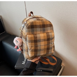 Close-up of yellow plaid backpack with a pink plush monster charm and brown leather strap