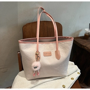 Detail of pink PU tote bag with heart embossing and cute plush toy charm on wooden chair