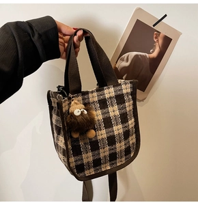 Detail of checkered tweed handbag with brown straps and cute monster plush pendant