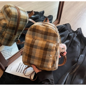 Detail view of mini plaid backpack with brown leather straps and pink pompom keychain