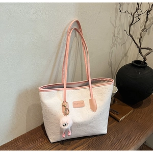 Detail view of cream tote bag with pink straps and embossed textures on a wooden table