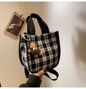 Detail of checkered canvas handbag with a cute brown monster plush doll charm attached