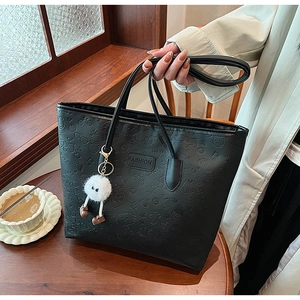 Detail of black embossed tote bag with creative plush charm and fashion label