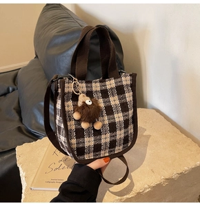 Detail of plaid canvas crossbody bag with dark handles and a plush monster charm