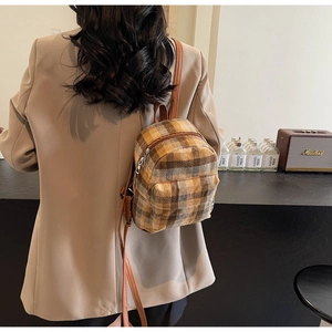 Close-up of the vintage brown plaid tweed texture and leather strap on a mini backpack