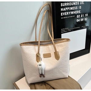 Close-up of cream tote bag featuring embossed fashion patterns and a plush charm